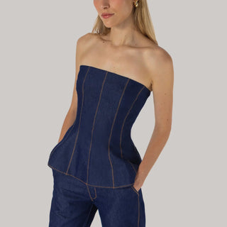 Woman wearing a strapless dark denim top with contrast stitching and matching denim pants, standing against a light gray background.