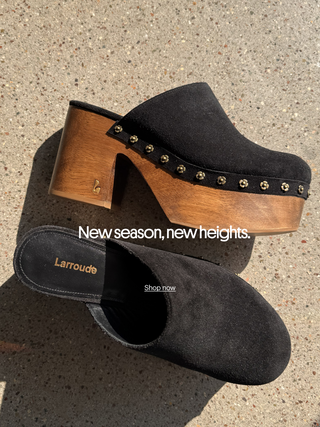 Black Larroudé platform mules with wooden heels and floral stud detailing photographed on a concrete surface, with “New season, new heights.”