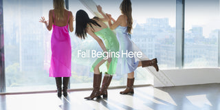 Three women in colorful dresses wearing Larroudé boots in a sunlit loft overlooking the city, with “Fall Begins Here” text.
