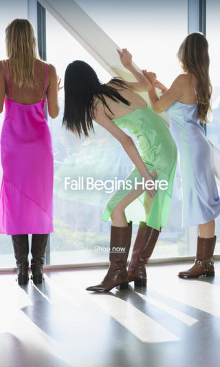Three women in colorful dresses wearing Larroudé boots in a sunlit loft overlooking the city, with “Fall Begins Here” text.