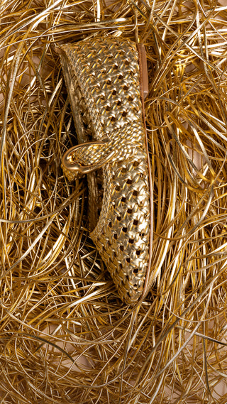Gold woven leather sandal placed on a background of tangled metallic gold cords.