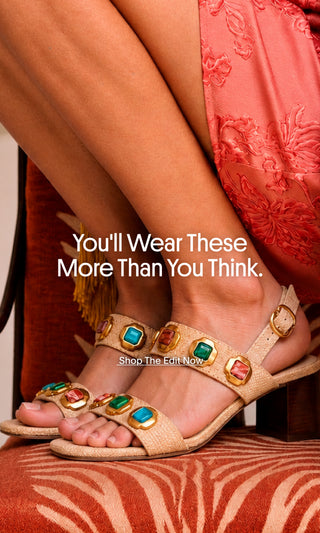 Close-up of a woman wearing embellished beige strappy sandals with colorful jewel details, paired with a coral floral dress. Text reads, “You’ll Wear These More Than You Think. Shop The Edit Now.